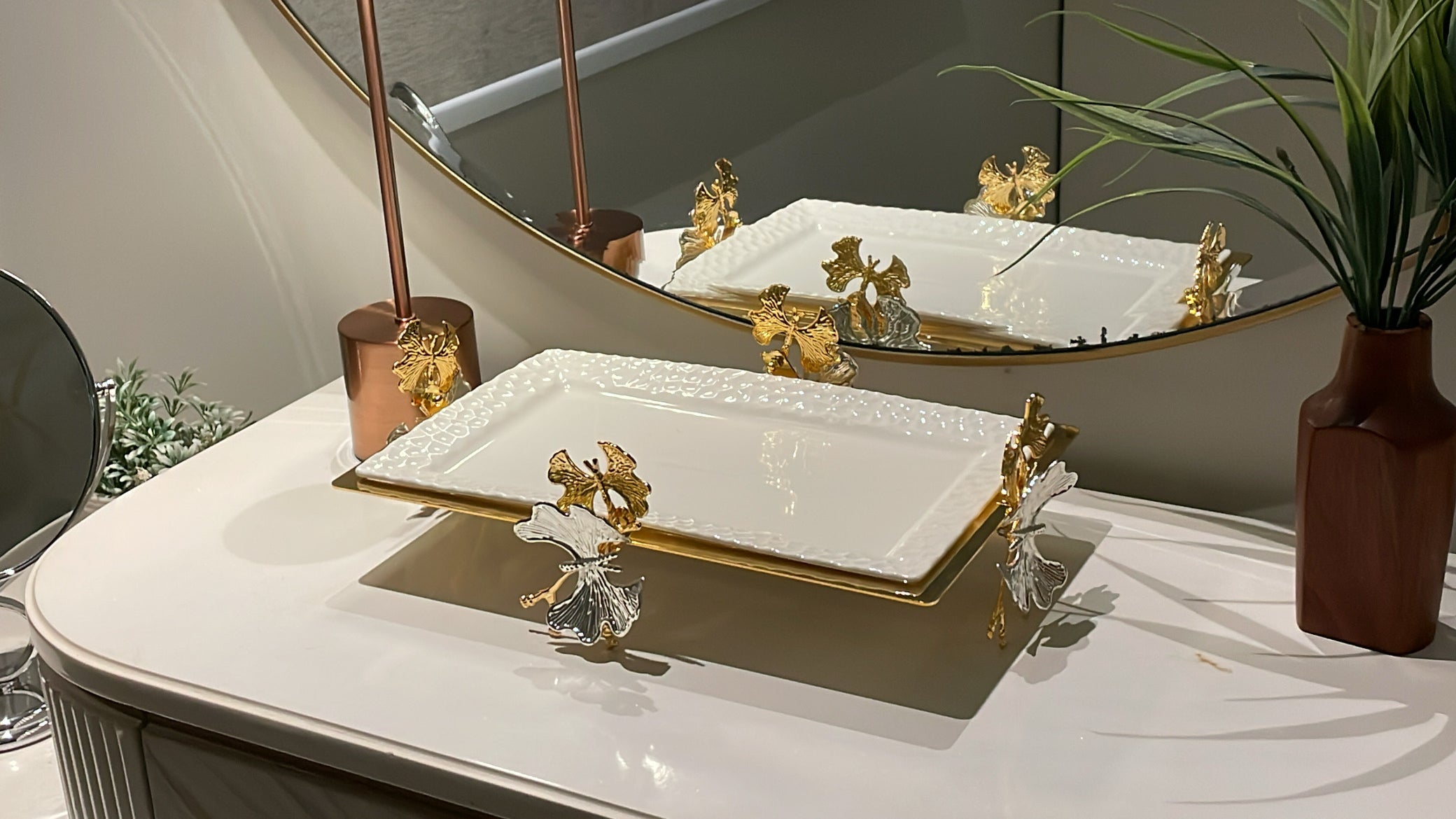 White ceramic dishes with gold accents, dried flowers, and greenery arranged on neutral background